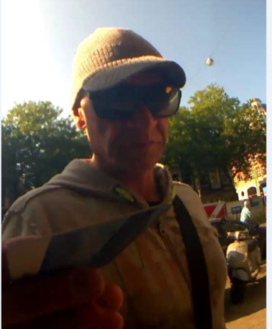 Man met grijze pet, zwarte zonnenbril en grijs vest aan.