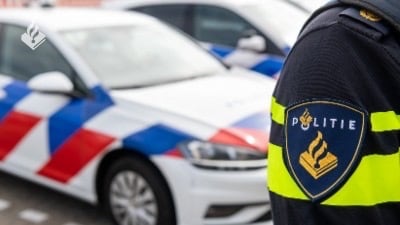 Politielogo op uniform met op de achtergrond een politieauto.