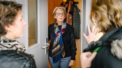 Vrouw doet deur open voor twee personen