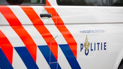 Politielogo op uniform met op de achtergrond een politieauto.