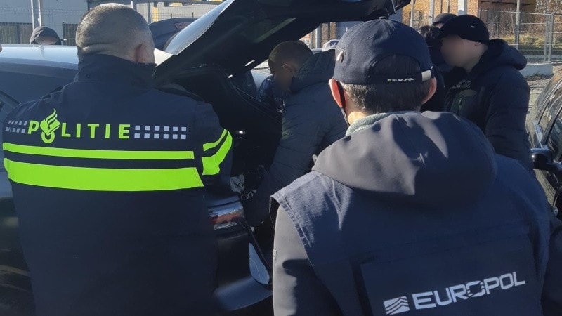 Agenten van de Nederlandse politie en Europol bij een auto waar iemand iets uit de achterbak pakt.