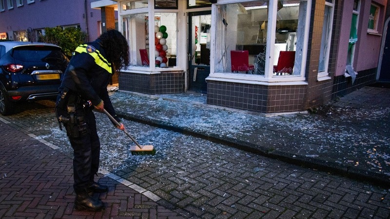 Een politiemedewerker ruimt de glassplinters op na een explosie bij een woning.