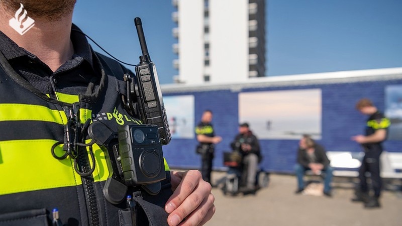 politieagent met bodycam zepcam T2+, op de achtergrond zijn collega's in gesprek met burgers, Foto: Politie